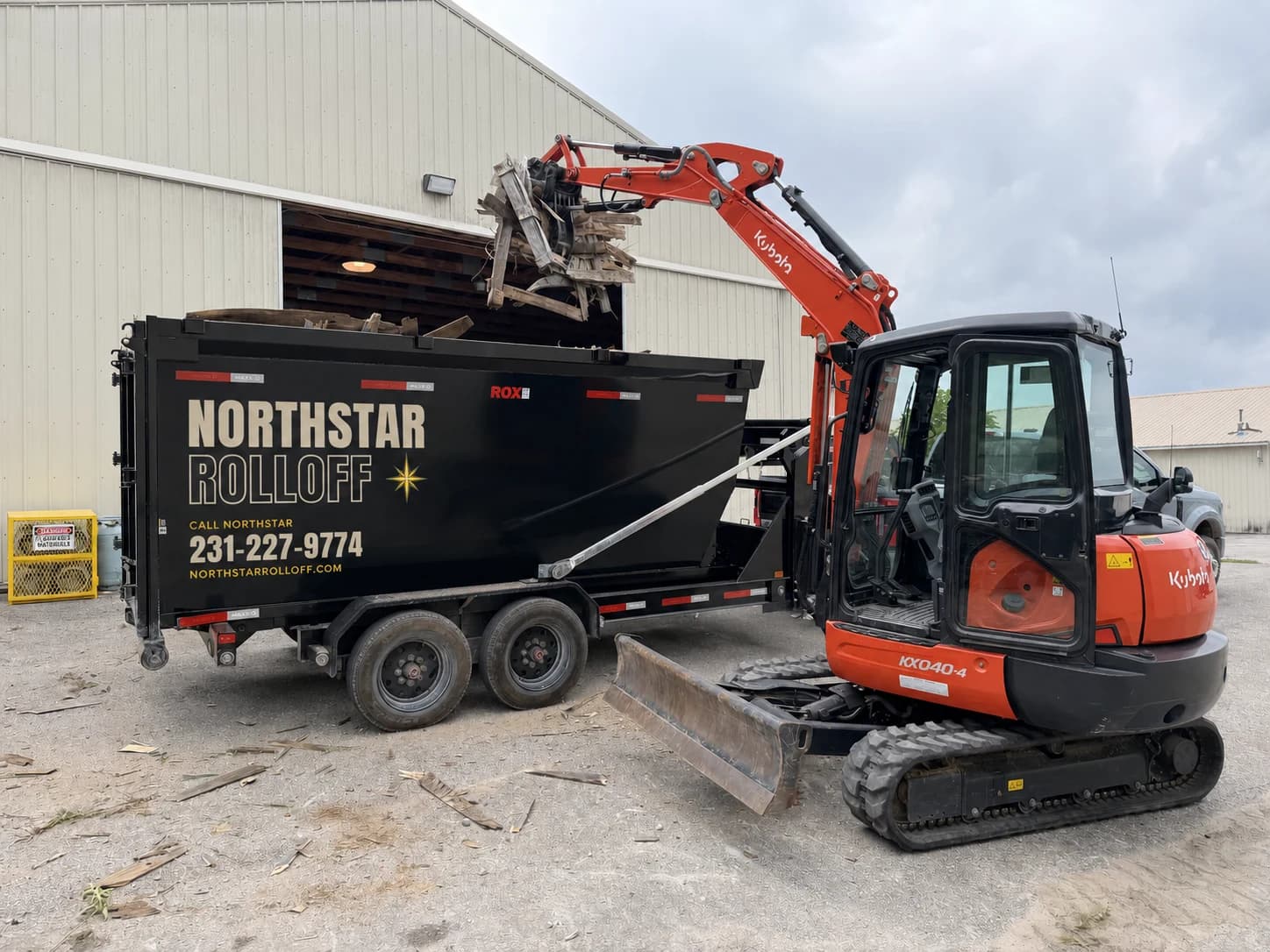 Excavator loading a branded Northstar roll-off dumpster